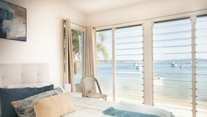 Une chambre à coucher avec un lit, une chaise et une grande fenêtre donnant sur la mer et les bateaux.