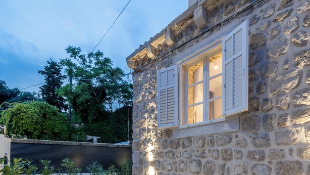 Un edificio de piedra con balcón, asientos al aire libre y una puerta que da a un espacio interior.
