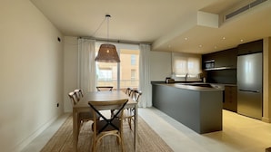 Une cuisine moderne dotée d’un îlot central, d’un coin repas avec une table et des chaises, et d’une grande fenêtre agrémentée de rideaux.