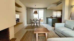 A modern living room with a sofa, a dining table with chairs, a kitchen area, and a large window with curtains.
