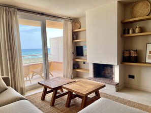 A living room with a wooden table, a sofa, a fireplace, a TV, and a view of the ocean.