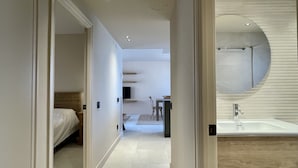 Une chambre d’hôtel moderne, dotée d’un lit, d’une salle de bain avec un grand miroir et d’un couloir menant à un espace repas.