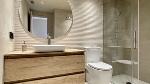 Ein modernes Badezimmer mit einem großen, ovalen Spiegel, einem Aufsatzwaschbecken, einer Toilette und einer Duschkabine.