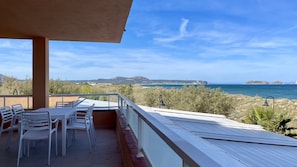 A balcony with a table and chairs, overlooking a coastal landscape with hills and the sea.