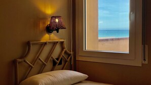 Ein Bett mit Kopfteil, eine Wandlampe und ein Fenster mit Blick aufs Meer.