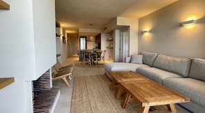 A modern living room with a sofa, wooden tables, and a dining area with chairs.