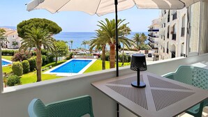 A balcony with a view of a swimming pool, palm trees, and a building with balconies.