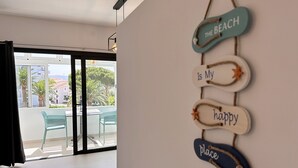 A room with a view of the beach, a sign on the wall, and a table with chairs.