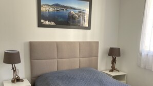Une chambre à coucher avec un grand lit, une table de chevet, une lampe, un tableau encadré au mur et une fenêtre avec des rideaux.
