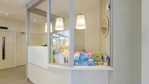 A reception area with a glass partition, a reception desk, and a display of brochures and magazines. - B&B HOTEL Antibes Juan-les-Pins (Antibes)