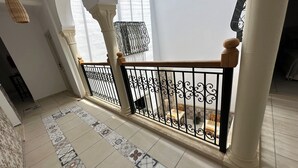 Een ruime hal met patroon tegels, een houten leuning en een zicht op een eetgedeelte met stoelen en een tafel.