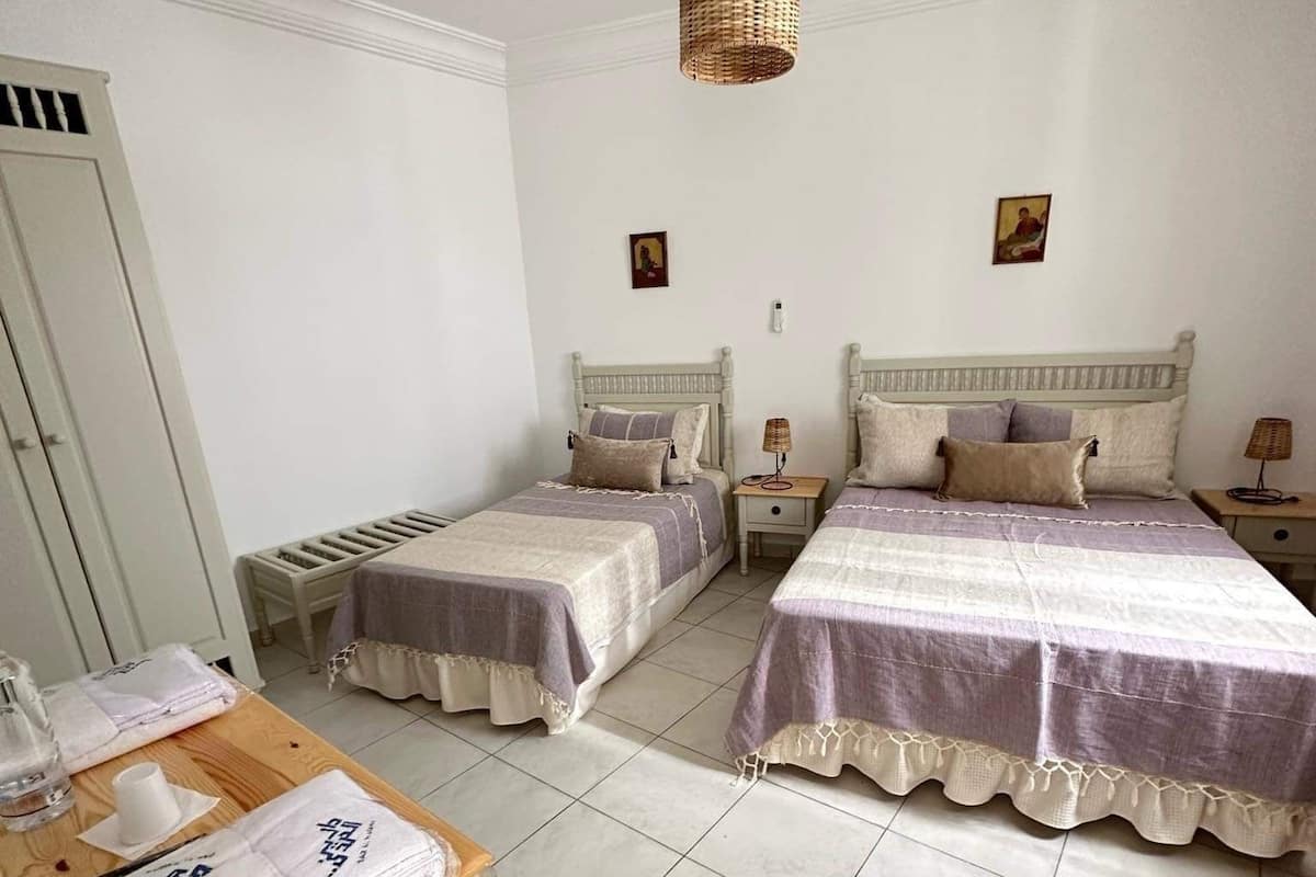 Quarto de hotel com duas camas de solteiro, uma mesa de madeira com toalhas e um lustre.