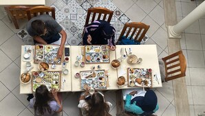 Een eetgedeelte met een betegelde vloer, houten stoelen en een tafel gedekt met diverse gerechten.