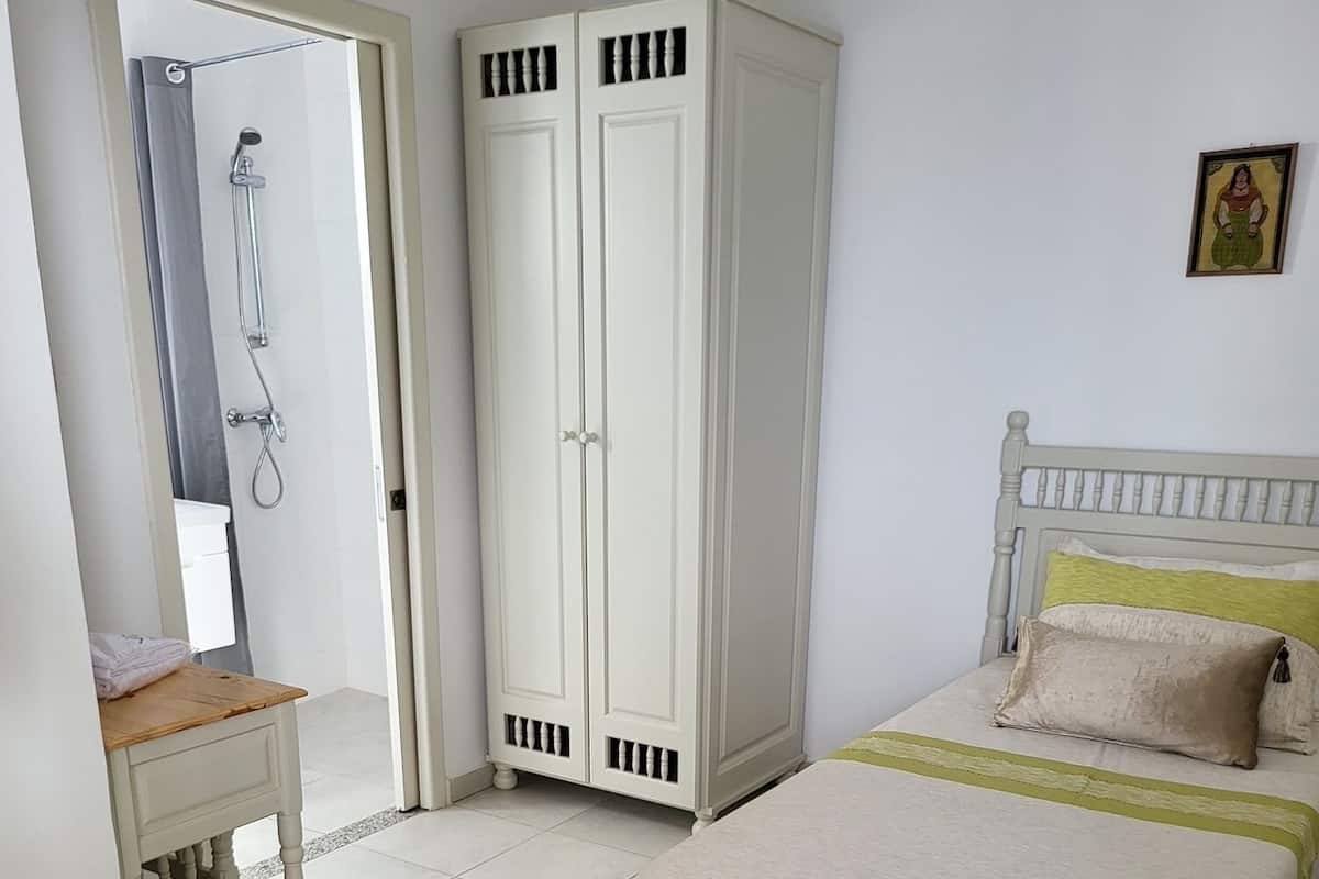 Quarto com cama, mesas de cabeceira, guarda-roupa e zona de duche.