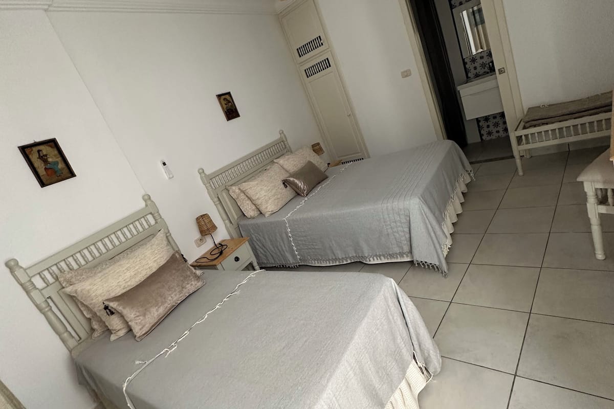 Quarto com duas camas, um guarda-roupa, um lustre e uma pequena mesa.