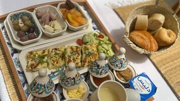 A tray with various food items including bread, cheese, olives, and dips, along with cups of coffee and a basket of pastries.