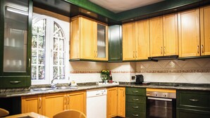 A kitchen with wooden cabinets, a dishwasher, an oven, and a window with a view of greenery. - Villa del Mamut, en Padul Granada (PADUL)