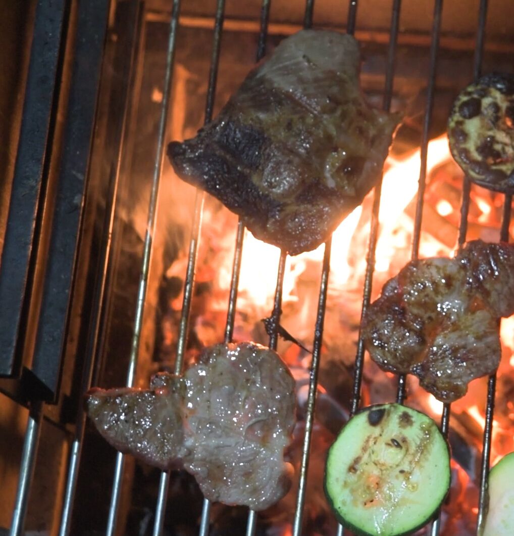 Ein Grill mit verschiedenen Fleisch- und Gemüsesorten, die über offenem Feuer gegart werden.