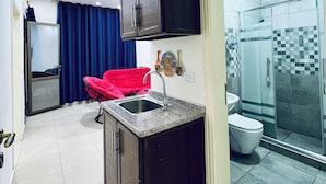 A compact kitchen with dark cabinets, a sink, and a red chair. - Petra Heaven (Wadi Musa)