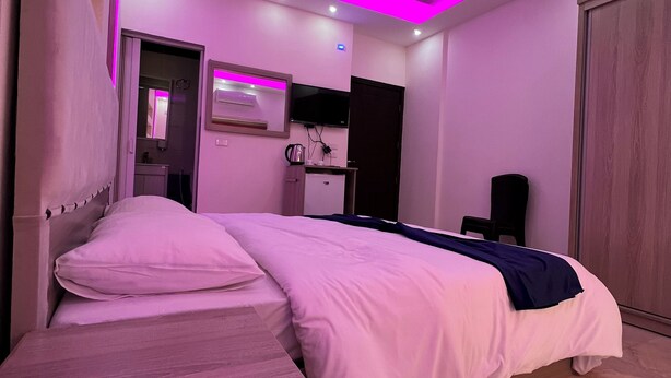 A modern bedroom with a bed, bedside table, and a TV mounted on the wall. - Petra Heaven (Wadi Musa)