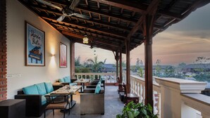 Un'area salotto esterna coperta con mobili in vimini, un'opera d'arte a tema pianoforte e vista sul paesaggio.