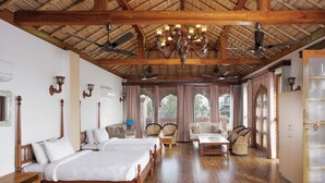 Un'ampia stanza con un letto grande, due letti più piccoli, un tavolo da pranzo e sedie. Sono presenti ventilatori a soffitto, un lampadario e ampie finestre con tende.