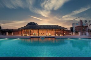 A swimming pool with lounge chairs and a thatched-roof pavilion. - Namaste Dwaar (Khatoli)
