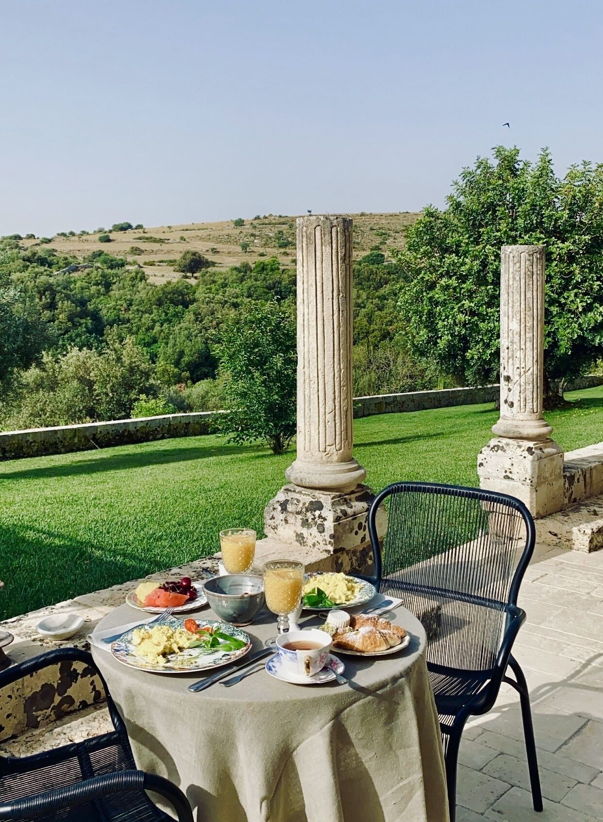 An outdoor dining table with a view of a green landscape and hills.
