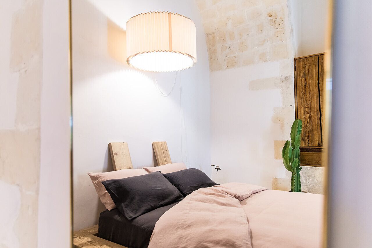 Un dormitorio con una cama, cabecera de madera, lámpara colgante y una planta de cactus.