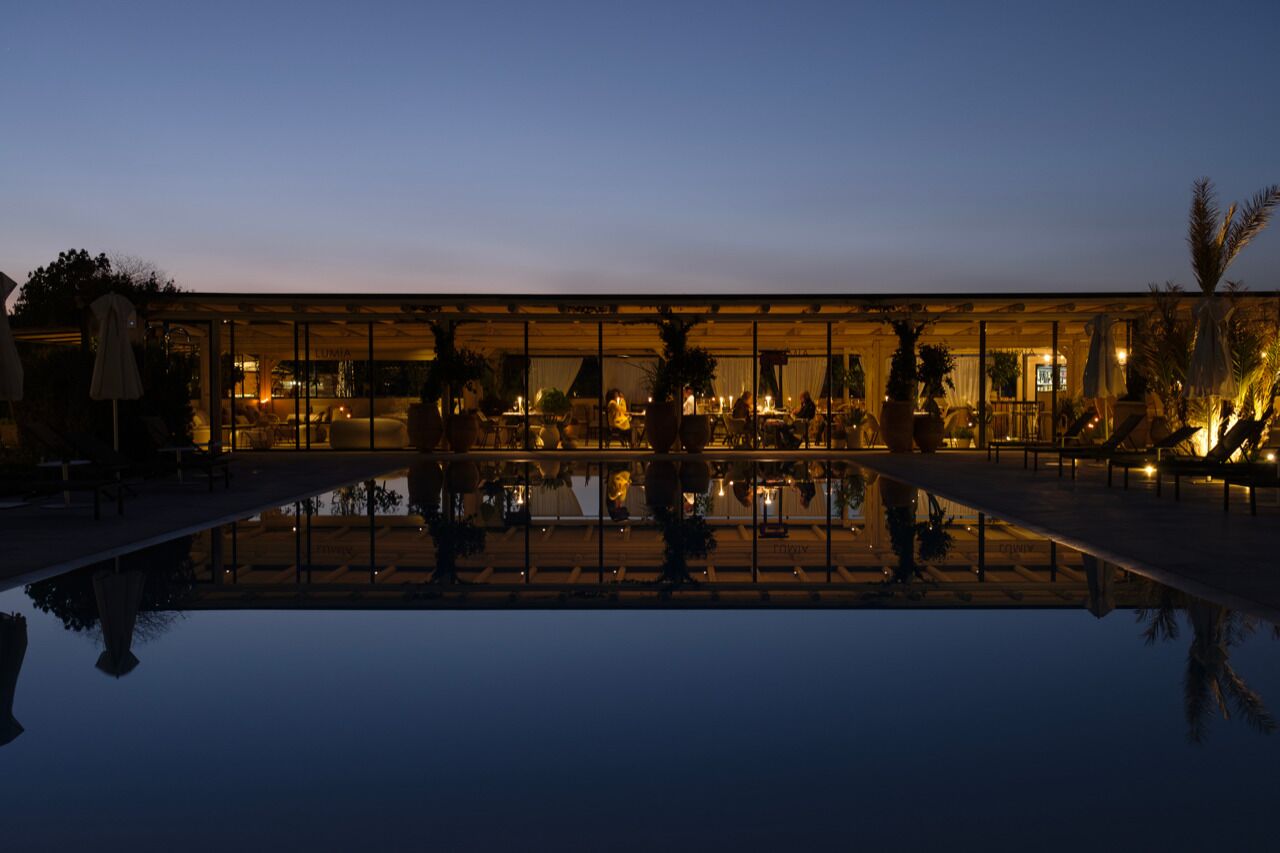 A modern building with a glass facade, a pool, and outdoor seating areas.