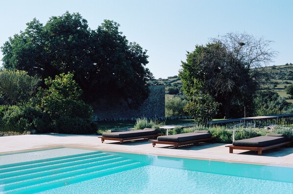 A pool with lounge chairs, surrounded by trees and a view of a hilly landscape. - Dimora delle Balze (Noto)
