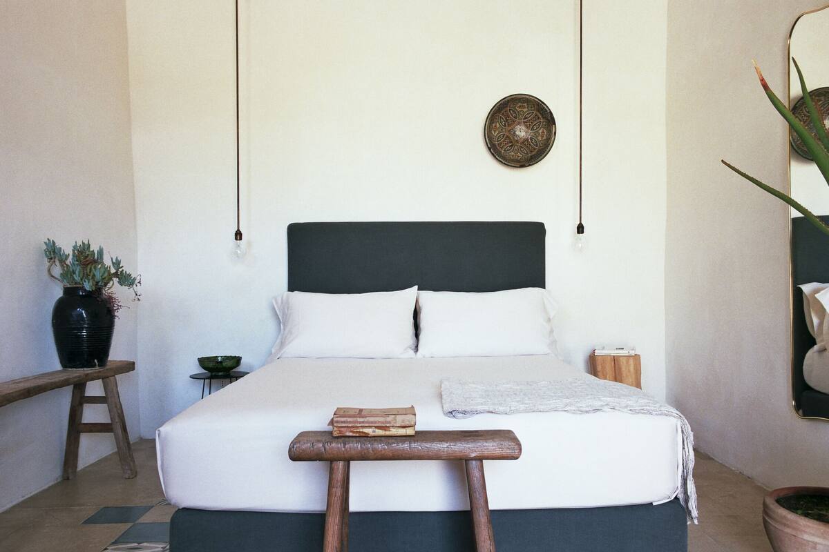 A neatly arranged bedroom with a bed, bedside tables, a small potted plant, and a decorative wall hanging.