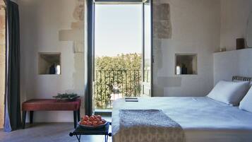 Ein Schlafzimmer mit einem großen Bett, einer Bank mit Orangen und Blick auf einen Balkon mit Bäumen.