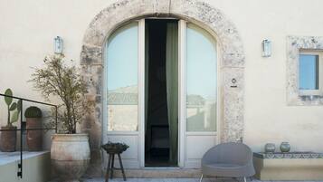 Une entrée d’immeuble avec une grande porte en arc de cercle, un pot de fleurs, une chaise et une petite table.