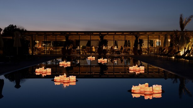 Un hotel lujoso con una piscina reflectante, un elegante espacio exterior para sentarse y un interior bien iluminado.