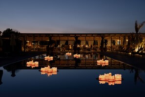Un hotel lujoso con una piscina reflectante, un elegante espacio exterior para sentarse y un interior bien iluminado.