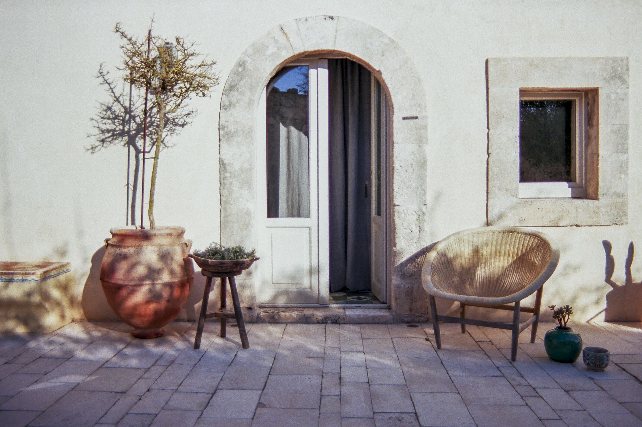 An outdoor area with a potted plant, a wicker chair, and a small table.