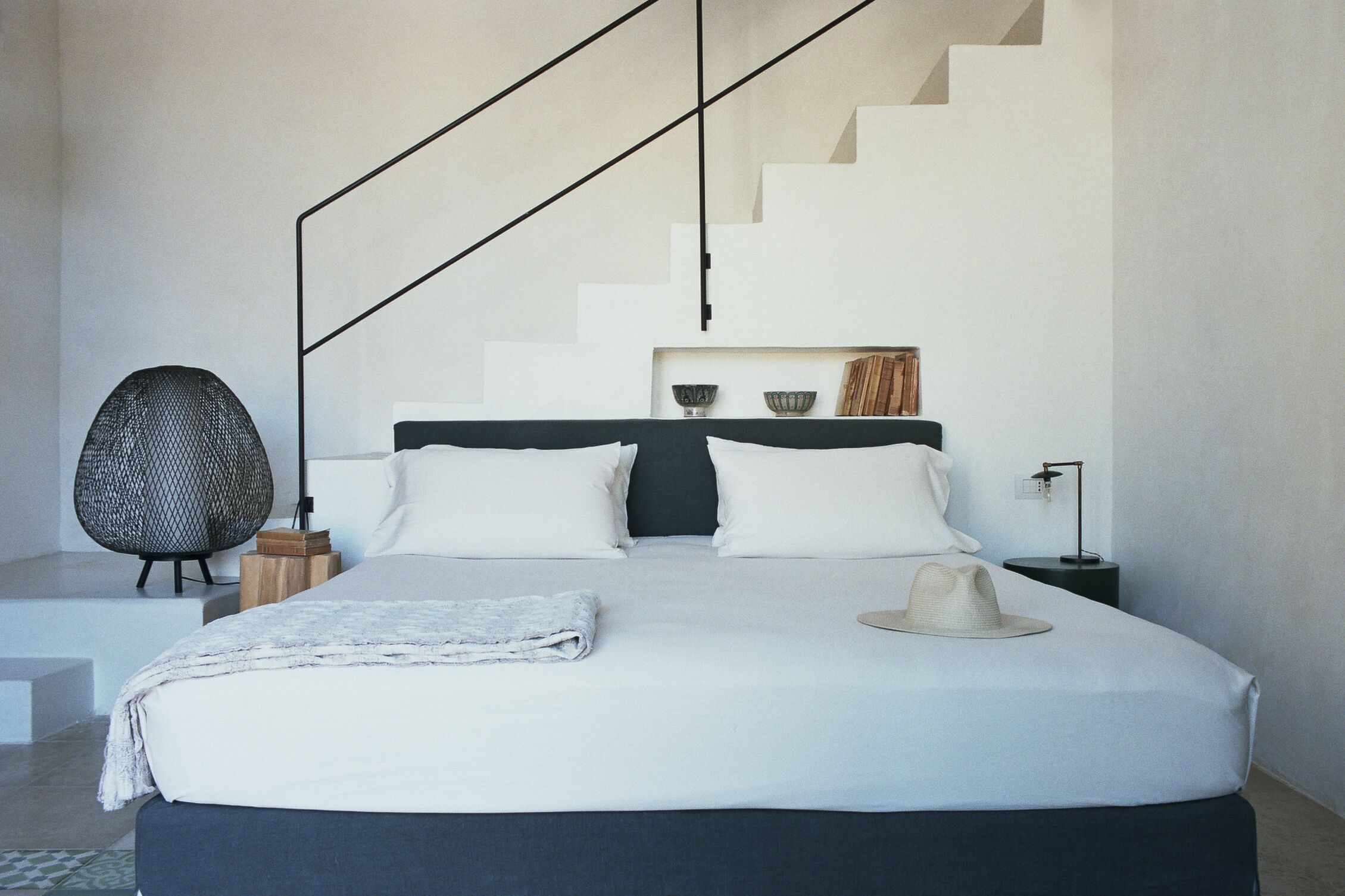 A modern bedroom with a large bed, a chair, a nightstand, and a staircase.