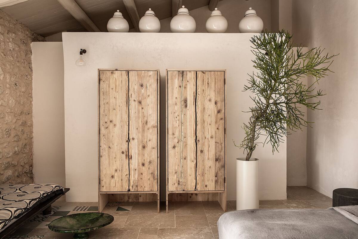 A room with a rustic wooden wardrobe, a potted plant, and a bench.