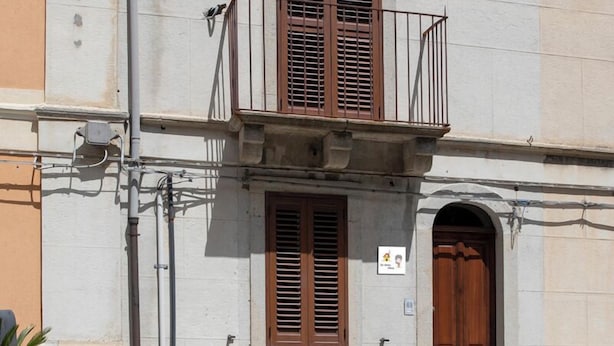 Un bâtiment doté d’un balcon, d’une porte en bois et d’une petite enseigne sur le mur.