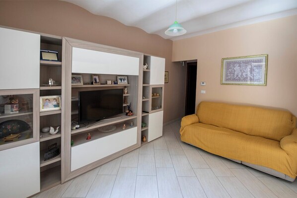 A living room with a sofa, TV, and shelves with various items. - Nonna Maria (Montalbano Elicona)