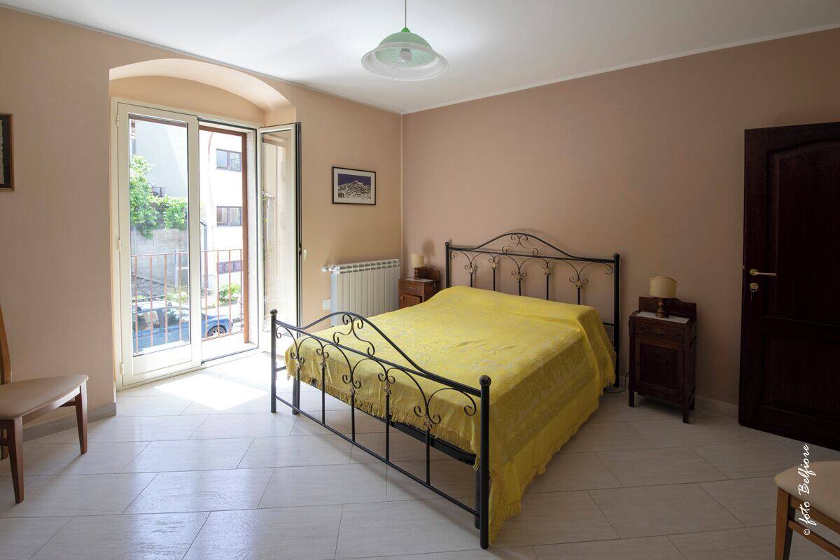 Een slaapkamer met een bed, een stoel, een nachtkastje, een deur en een raam.