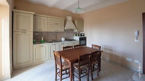 Une cuisine avec des meubles de couleur beige, un pare-feu en carrelage, une table à manger en bois avec des chaises et un luminaire suspendu.