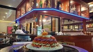 A bar area with a central display of a layered vegetable dish, surrounded by shelves of liquor bottles and glasses. - Garden Phuket Hotel (Patong)
