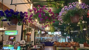 An indoor restaurant with hanging flower arrangements, tables, chairs, and a bar area. - Garden Phuket Hotel (Patong)
