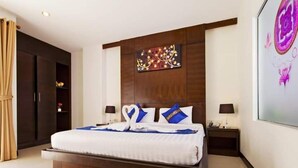 A modern hotel room with a large bed, two bedside tables, a wardrobe, and a decorative wall piece. - Garden Phuket Hotel (Patong)