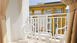 A balcony with white plastic chairs and a small table, overlooking a yellow building with white railings. - Garden Phuket Hotel (Patong)