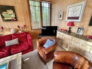 Uma sala de estar aconchegante com um sofá vermelho, poltrona de couro e uma televisão.