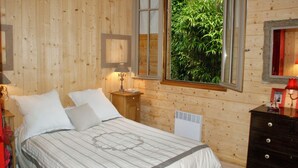 Habitación con paneles de madera, con una cama, mesita de noche, lámpara y ventana con vistas a la vegetación.