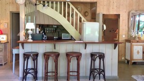 Un interior de madera con una zona de bar, tres taburetes, un microondas y un refrigerador.